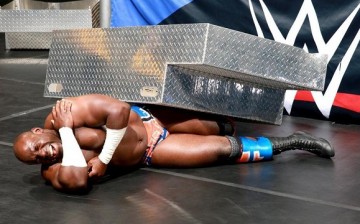 Apollo Crews cringes in pain after Sheamus hits him with the steel steps.