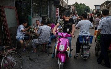 A Chinese man riding on his electric scooter passed a group of men eating at an outdoor restaurant on May 27, 2015 in Beijing, China.