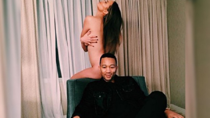 Teigen, who is completely naked, uses her hands to cover her breast.