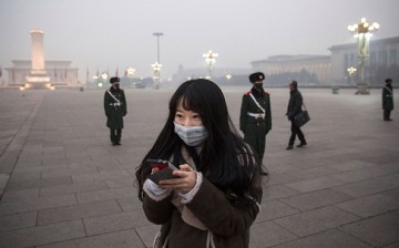 A Chinese woman looks at her phone as Chinese Paramilitary police wear masks to protect against pollution as they stand guard in heavy smog in Tiananmen Square on Dec. 9, 2015 in Beijing, China.