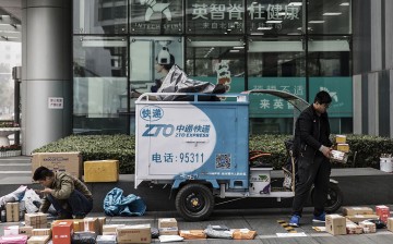 Delivery personnel sort out parcels beside a ZTO Express Delivery vehicle in Beijing.