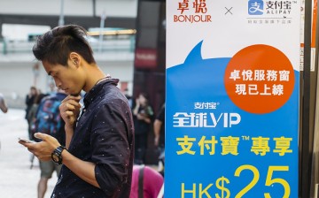 A man with a smartphone stands beside an advertisement for Alipay in a Hong Kong store.