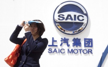 A woman takes a selfie beside a logo of SAIC, China's largest auto manufacturer, during an auto show in Beijing.
