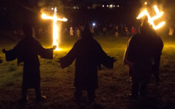 Ku Klux Klan members burn a wooden cross and a swastika.