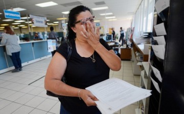 Woman holds job fliers and wipes away tears as she becomes emotional after getting laid off from her current job.