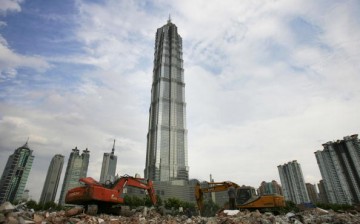 Scrapers scoop ruins at a demolition site of old houses in front of the Jinmao Tower, China's tallest building, on July 5, 2005 in Shanghai, China.