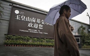 A man holding an umbrella walks past a welcome sign for Yuhuang Shannan Fund Town in Hangzhou, China.