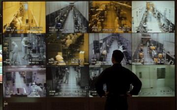 A man observes semiconductor manufacturing on wall of monitors.