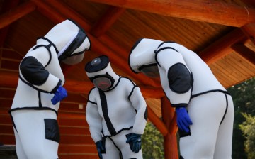 Jake Bodart (L), Austin Johnson (C) and Jessica Rendon (L) of the Oregon Department of Agriculture look down at their attached boots while wearing hornet extraction suits, 