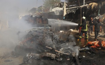 A member of a fire crew sprays water onto a burned vehicle after a car bomb exploded in Afrin, Syria,