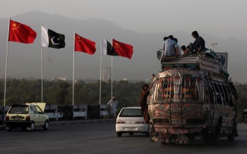 People sit on top of a bus as they go past flags of Pakistan and China displayed along a road in Islamabad. 