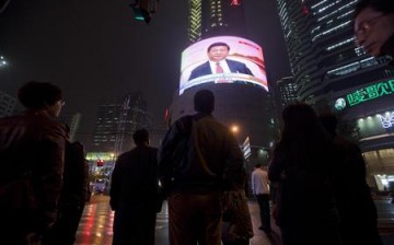 People in China watch a huge public TV screen showing a news broadcast. 