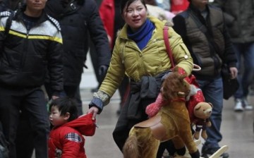 A woman holds her child with one hand and toys with the other at a railway station in Beijing, Jan. 14, 2014.