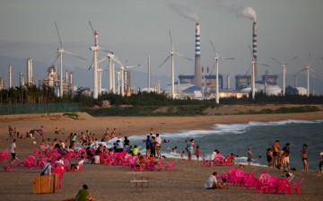 Windmills and a power plant can be seen in the distance as beachgoers watch sunset in the city of Dongfang on the western side of China's island province of Hainan.