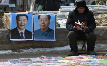 A book vendor reads a book as he waits for customers next to portraits of Chinese President Xi Jinping (L) and late Chairman Mao Zedong, in Juancheng county, Shandong Province, Jan. 30, 2015.