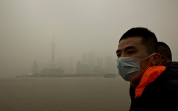 A man wears a face mask while walking on the Bund in front of the financial district of Pudong during a hazy day in downtown Shanghai.