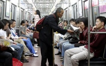 An elderly beggar tries to solicit money from subway passengers on a Beijing subway train. 