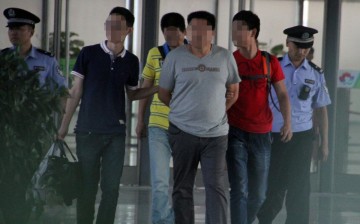 The suspected leader of a gang that allegedly hired university students to impersonate test takers for the gaokao is escorted by officers in a train station in Heze City, Shandong Province, on June 8.