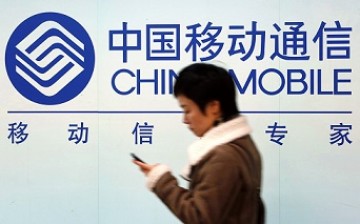 A woman walks past a billboard of China Mobile, one of China's top three telecom operators. 