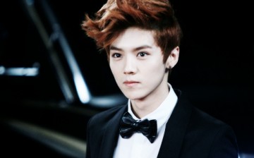 Lu Han, wearing an earring, poses for the camera in a suit and bowtie.