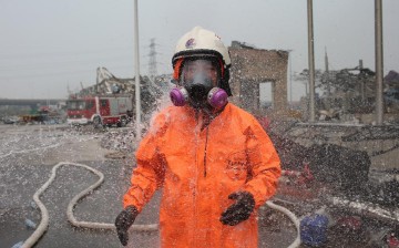 A firefighter wearing chemical protective clothing is sterilized at the site of explosion in Tianjin, north China, Aug. 15, 2015. 