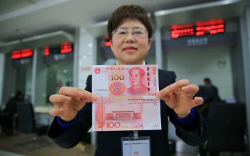 A bank employee shows both sides of the new 100 yuan note in Anqing, Anhui Province, on Nov. 12, 2015.