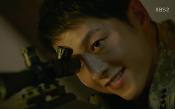 Captain Yoo Shi Jin, played by Song Joong-ki, is using his rifle scope to spy on Dr. Mo Yeon (Song Hye-Kyo) while washing her face outside the base camp.