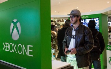 A man plays an XBox One while waiting in line to buy a unit of the game console from a Microsoft store. 