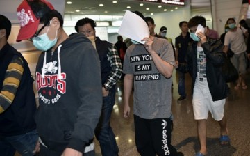 Alleged fraud suspects try to conceal their identities by wearing a face mask as policemen escort them when they arrive at Taoyuan Airport in Taoyuan on April 15, 2016.