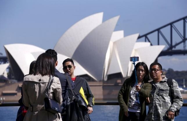 Chinese tourists take pictures of themselves with the Sydney Opera House in the background.