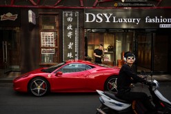 A Chinese man stands next to his luxury car as its is parked in an upscale shopping district on May 29, 2015, in Beijing, China. 