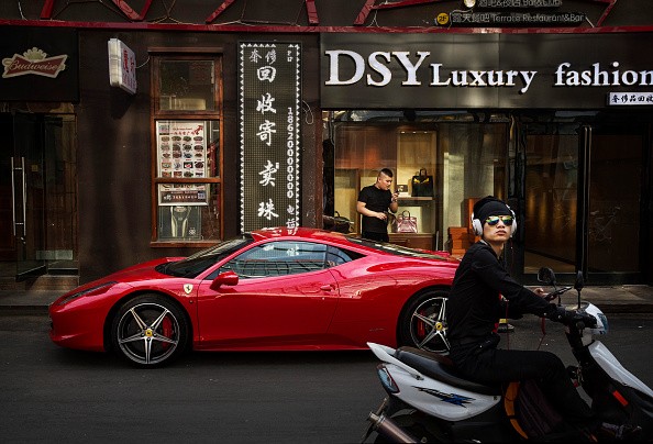A Chinese man stands next to his luxury car as its is parked in an upscale shopping district on May 29, 2015, in Beijing, China. 