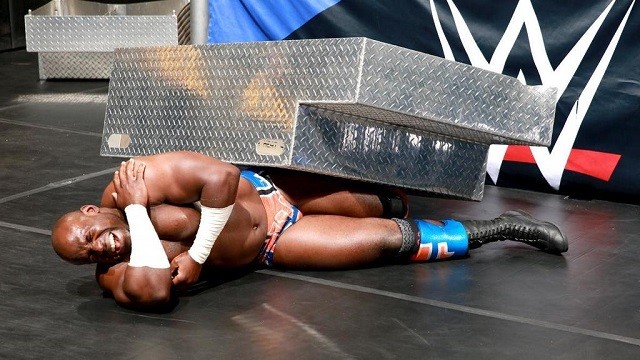 Apollo Crews cringes in pain after Sheamus hits him with the steel steps.