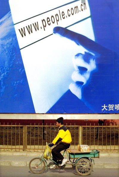 A man pedals his tricycle in front of a billboard featuring an advertisement for a Chinese official website Jan. 30, 2002 in Beijing, China. 