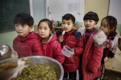 Children of migrant parents wait in line for lunch in school.