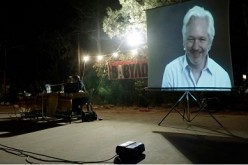 Julian Assange is projected onto a screen as he speaks  via livestream at a video conference in Greece.