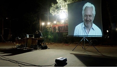 Julian Assange is projected onto a screen as he speaks  via livestream at a video conference in Greece.