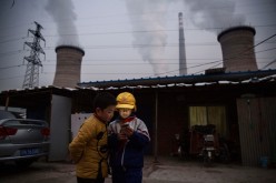 Chinese boys look at their smartphone in front of their house next to a coal-fired power plant on Nov. 27, 2015, on the outskirts of Beijing, China.