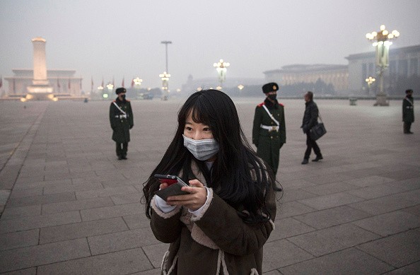 A Chinese woman looks at her phone as Chinese Paramilitary police wear masks to protect against pollution as they stand guard in heavy smog in Tiananmen Square on Dec. 9, 2015 in Beijing, China.