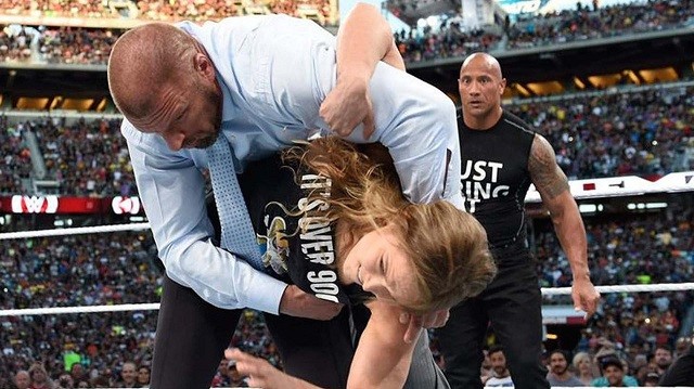 Ronda Rousey executes a Judo throw to Triple H as The Rock looks on at WrestleMania 31 last year. 