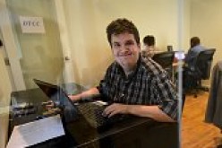 Young man looks cheerfully working on a laptop who was earlier diagnosed with autism in his childhood.