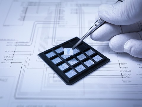 An electronic chip held with a pair of tweezers.