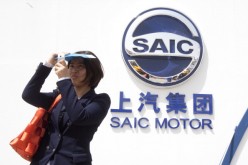 A woman takes a selfie beside a logo of SAIC, China's largest auto manufacturer, during an auto show in Beijing.