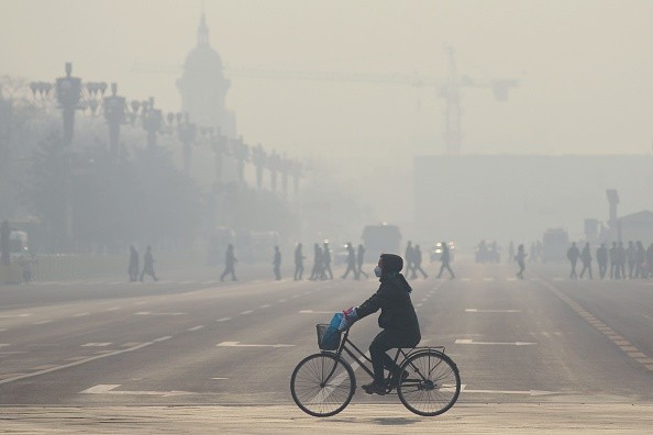  A woman wears a mask as she rides her bicycle along a street near Tiananmen Square on the third day of a red alert for pollution in Beijing.