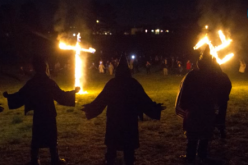 Ku Klux Klan members burn a wooden cross and a swastika.