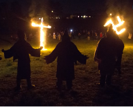 Ku Klux Klan members burn a wooden cross and a swastika.