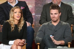 Katie Cassidy speaks as Stephen Amell listens onstage during the 'Arrow' and 'The Flash' panel as part of The CW 2015 Winter Television Critics Association press tour.