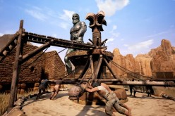 An Avatar striding through a village, right in front of a group of thralls pushing the Wheel of Pain in 'Conan Exiles.'