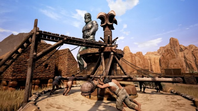 An Avatar striding through a village, right in front of a group of thralls pushing the Wheel of Pain in 'Conan Exiles.'