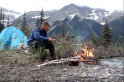 A man sits in front of a bonefire while being one with nature. 